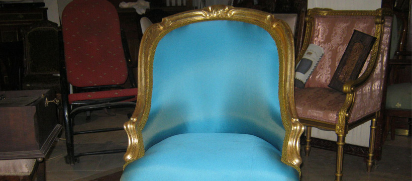 Odrestaurowany fotel w stylu Ludwika XVI z turkusową tapicerką i złoconymi zdobieniami, widoczny w otoczeniu innych mebli.
