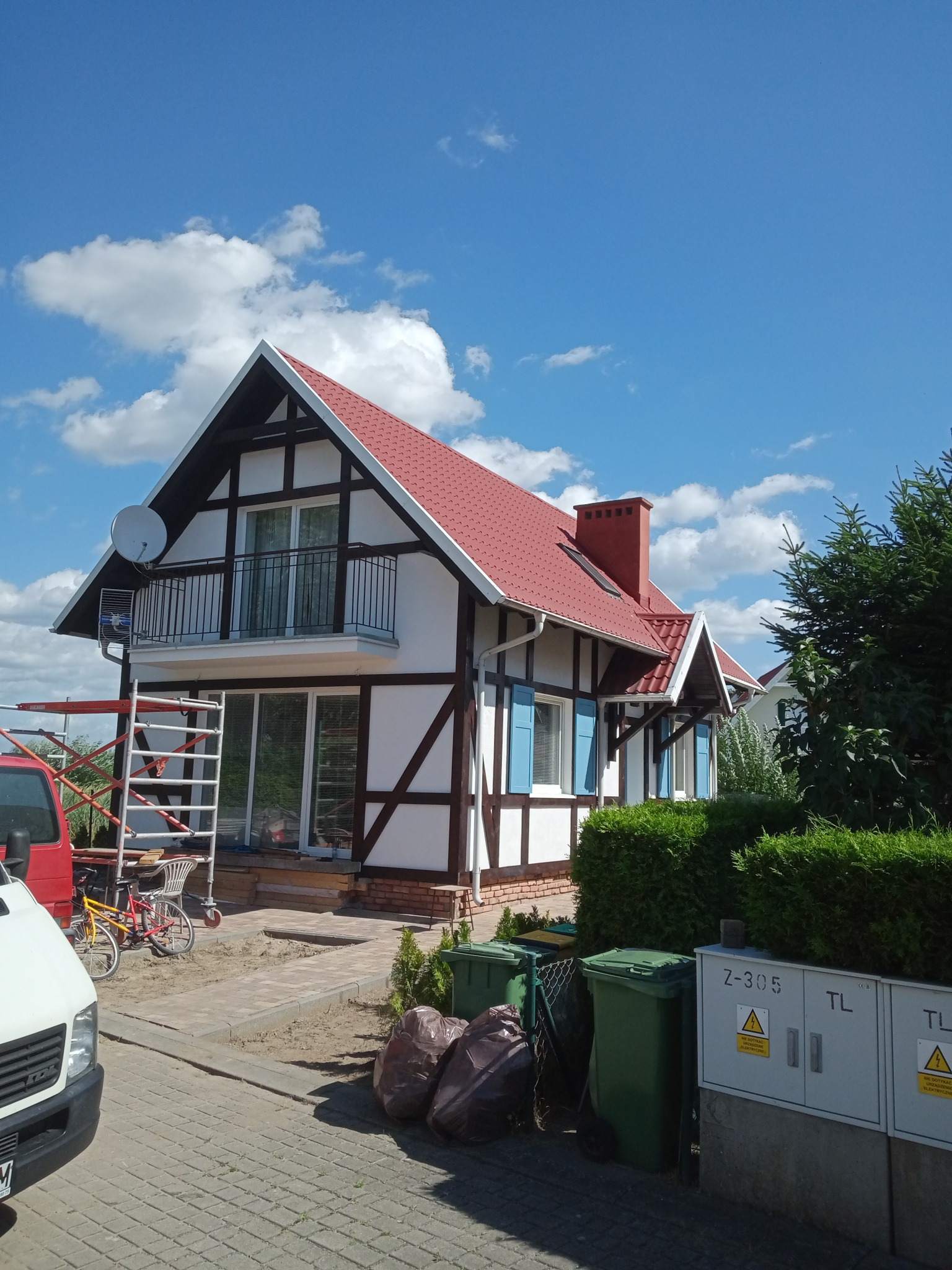 Dom w stylu szachulcowym w Kołczygłowach z nowym czerwonym dachem, widoczne rusztowanie i samochody dostawcze sugerujące prace budowlane.