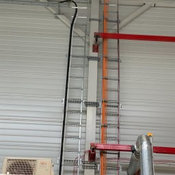 Time to Start (Danylo Chernytsia) - Wewnętrzna instalacja elektryczna w hali produkcyjnej: kable w korytach, rury wentylacyjne i klimatyzator Fujitsu na tle blachy trapezowej.