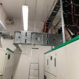 Time to Start (Danylo Chernytsia) - Wnętrze rozdzielni elektrycznej z korytem kablowym pod sufitem, widoczna drabina aluminiowa i szafy sterownicze z zielonymi akcentami, oświetlenie jarzeniowe.