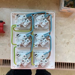 Time to Start (Danylo Chernytsia) - Cztery gniazda elektryczne w białej ramce, połączone przewodami: niebieskim, brązowym i żółto-zielonym, widoczne śruby mocujące, obok pudełko z akcesoriami marki Simon.