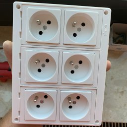 Time to Start (Danylo Chernytsia) - Biała, potrójna ramka gniazd elektrycznych marki Simon, trzymana w dłoni, widoczne detale gniazd z bolcem uziemiającym.