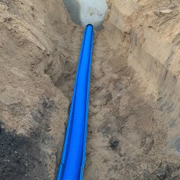 Time to Start (Danylo Chernytsia) - Niebieska rura karbowana w wykopie z piasku, zabezpieczona niebieską osłoną, widoczny fragment fundamentu budynku.