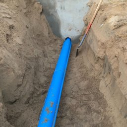 Time to Start (Danylo Chernytsia) - Niebieska rura kanalizacyjna ułożona w wykopie ziemnym, widoczna szpadel oparty o ścianę wykopu i fragment betonowej konstrukcji.