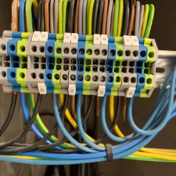 Szczegółowe ujęcie panelu elektrycznego z wieloma kolorowymi przewodami podłączonymi do listew zaciskowych na szynie DIN, numery na zaciskach wskazują porządek połączeń.