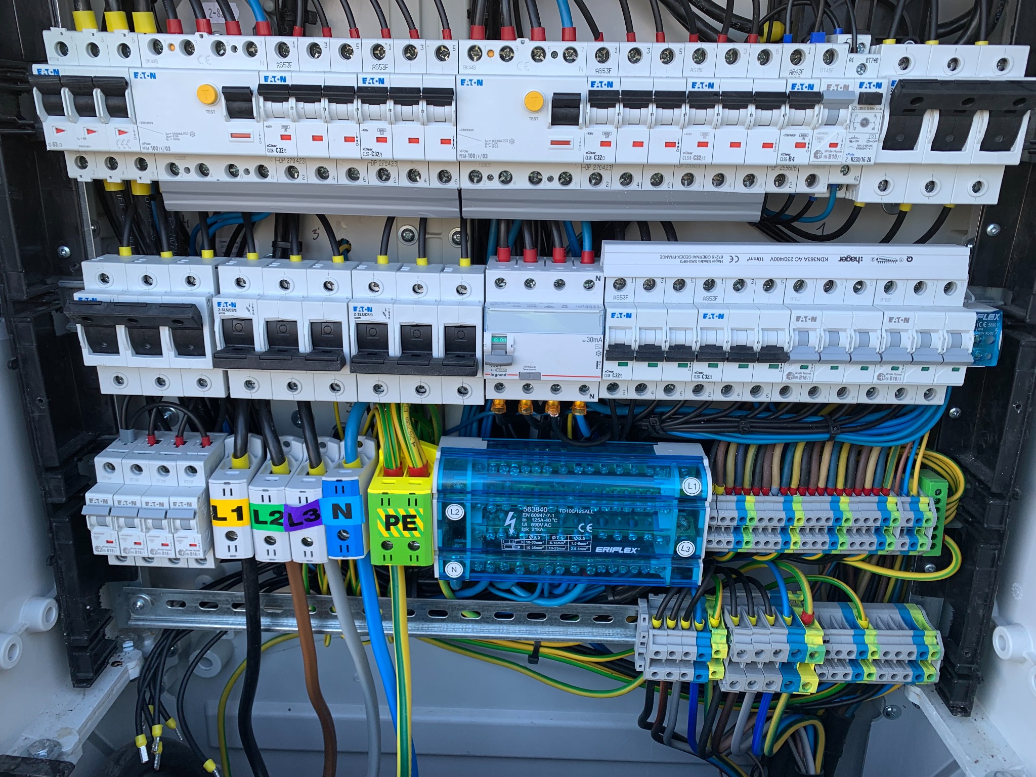 Otwarta skrzynka elektryczna z widocznymi zabezpieczeniami Eaton, bezpiecznikami, przewodami oznaczonymi L1, L2, L3, N, PE oraz niebieskim modułem Eriflex, uporządkowany układ przewodów i złączek.