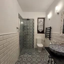 Wykończona łazienka z kabiną prysznicową z wzorzystymi płytkami, umywalką w stylu retro na metalowej podstawie i białymi płytkami ściennymi typu metro.