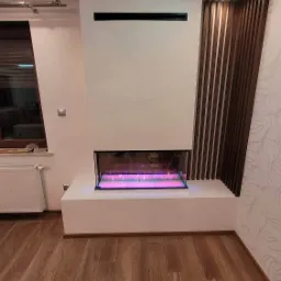 Nowoczesny biokominek w zabudowie z płyt kartonowo-gipsowych, obok dekoracyjna ściana z drewnianych listew, na podłodze panele.