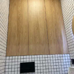 Zabudowa nad geberitem w łazience, fronty z płyty meblowej Egger Dąb Hikora, wnętrze w kolorze popielatym, półki z regulacją wysokości, ściany wyłożone białą mozaiką z czarną fugą.