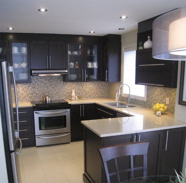 Nowoczesna kuchnia z ciemnymi szafkami, mozaikową ścianą nad blatem i jasnym blatem roboczym oraz wyspą, oświetlona punktowymi lampami sufitowymi.