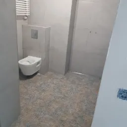 Nowoczesna łazienka z podwieszaną toaletą, grzejnikiem drabinkowym i płytkami podłogowymi w stylu vintage, widok z rogu pomieszczenia.