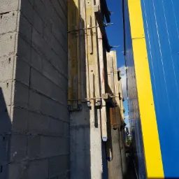 Szare bloczki fundamentowe z drewnianym szalunkiem i żółto-niebieskim panelem w tle, widok z dołu.