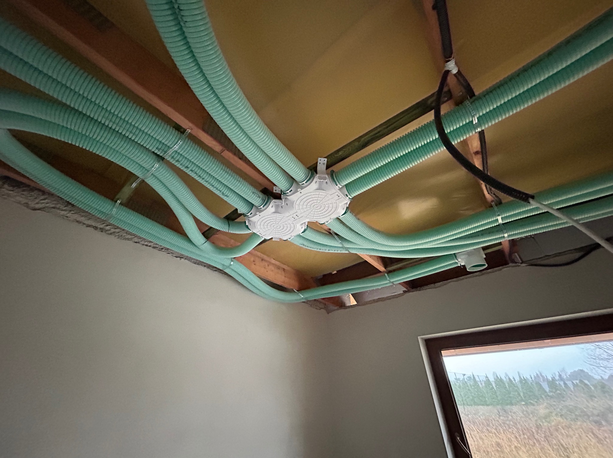 Rozprowadzenie instalacji rekuperacji pod stropem z widoczną skrzynką rozdzielczą i przewodami wentylacyjnymi w kolorze miętowym, mocowanymi do drewnianych belek stropowych.