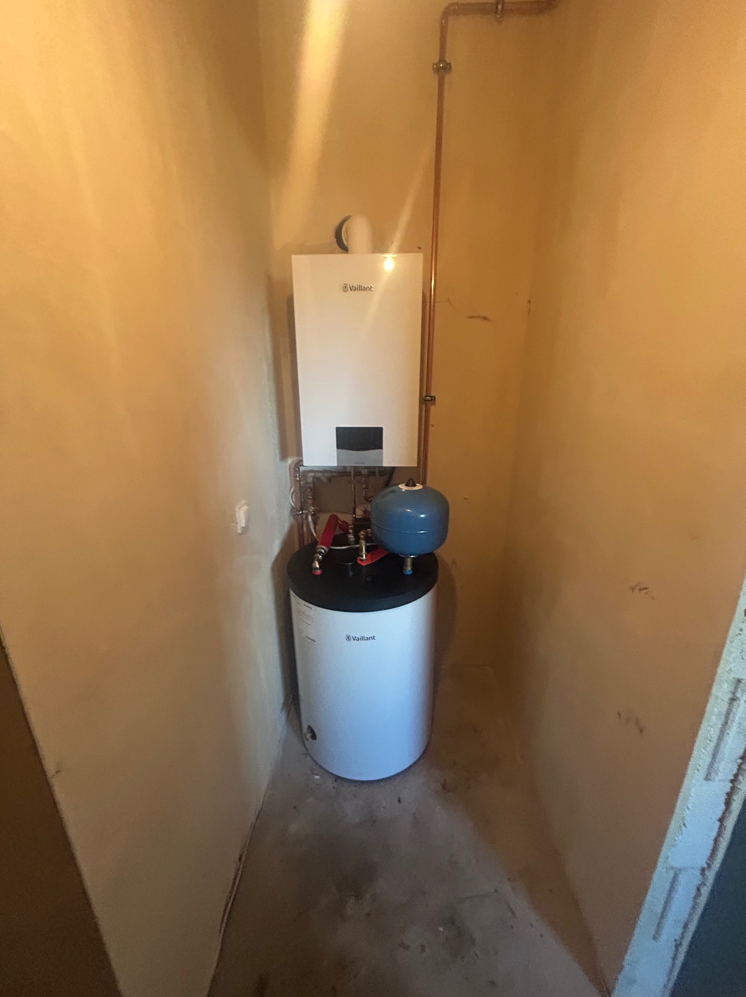 Piec gazowy marki Vaillant z niebieskim zbiornikiem wyrównawczym, zainstalowany w pomieszczeniu o beżowych ścianach w Bogdańcu, z widocznymi miedzianymi rurami.