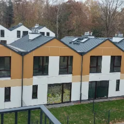 Nowoczesne szeregowe domy z dużymi oknami i szarym dachem, widok z balkonu na osiedle w jesiennej scenerii.