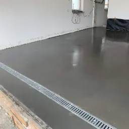 Świeżo wylana, gładka posadzka z widocznym odpływem liniowym w pomieszczeniu w trakcie prac wykończeniowych.