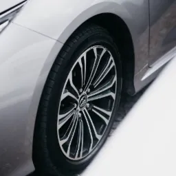 Srebrny samochód z aluminiowymi felgami i oponami na śniegu, widok z bliska na przednie koło i reflektor.