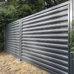 Nowoczesna, pozioma brama przesuwna w kolorze grafitowym, z widocznym zamkiem, na tle zieleni drzew.