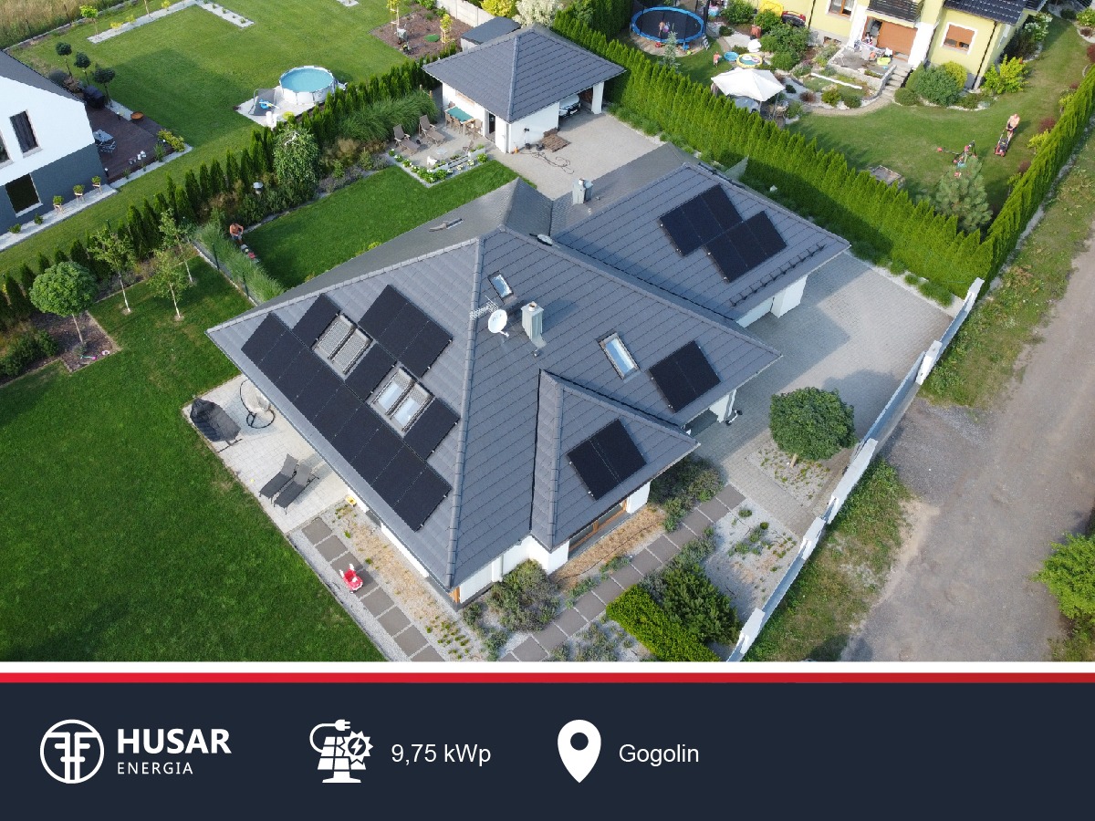 Widok z drona na dom z szarym dachem i panelami słonecznymi, zadbany ogród z basenem w tle.