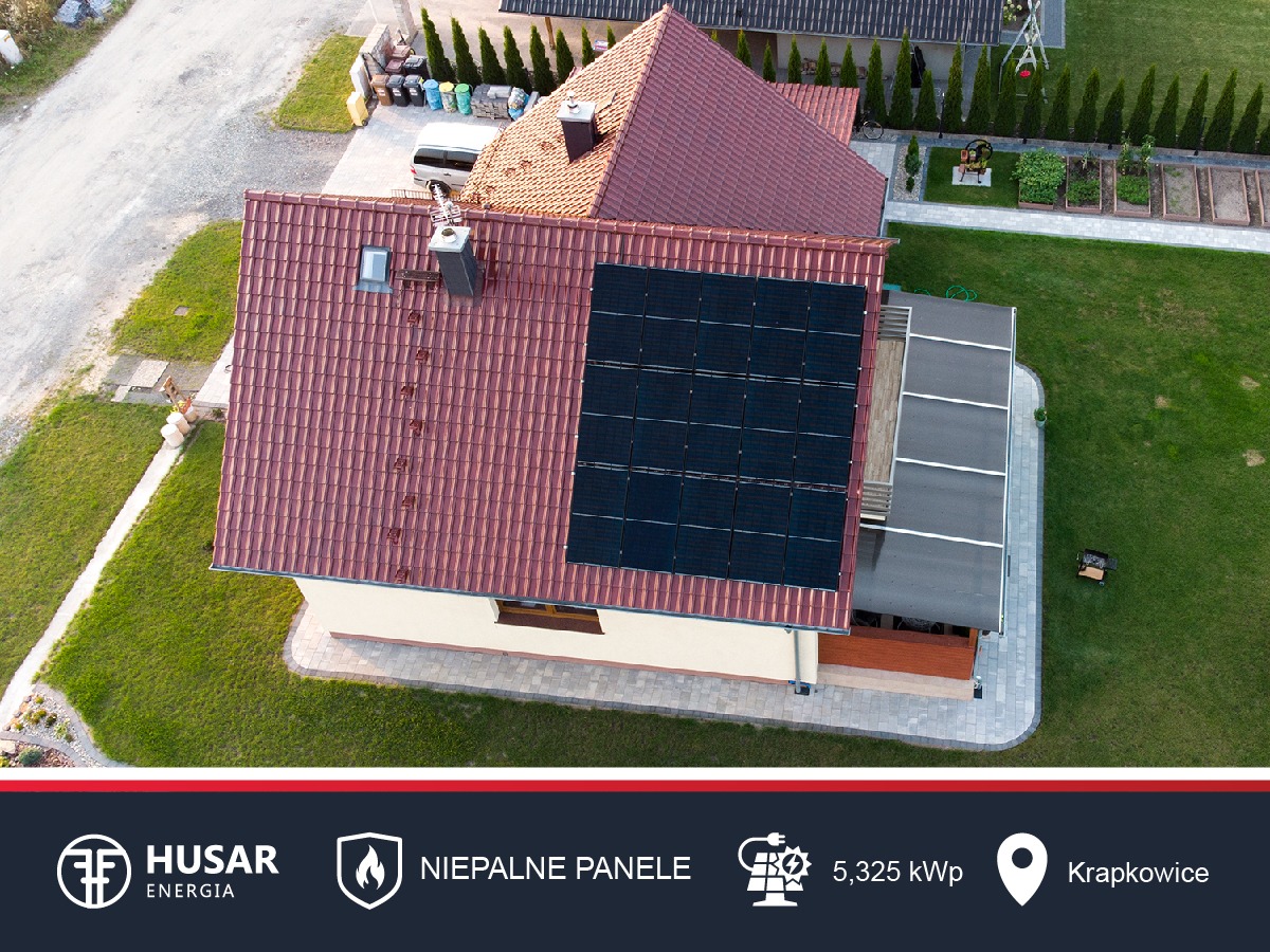 Widok z góry na dom z czerwoną dachówką i zainstalowanymi panelami słonecznymi, widoczny ogród i otoczenie domu.