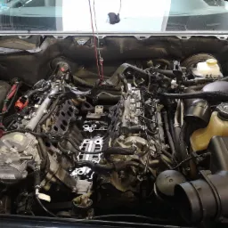 Widok z góry na rozmontowany silnik samochodowy w trakcie naprawy, z widocznymi przewodami, wężami i elementami konstrukcyjnymi.