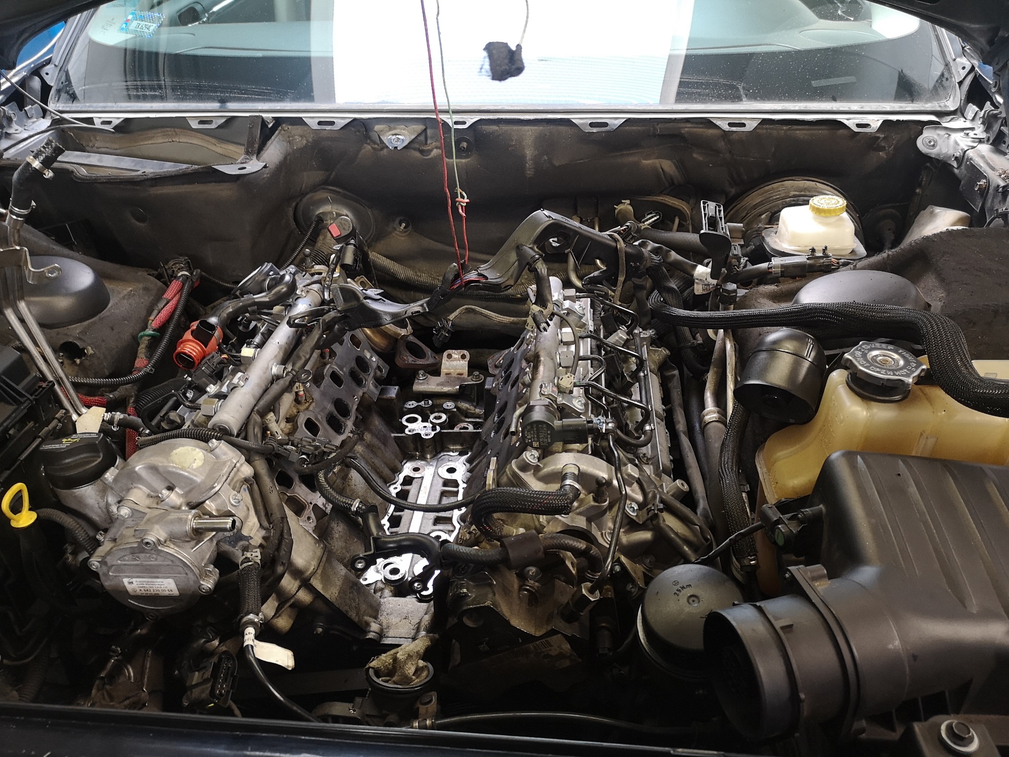 Widok z góry na rozmontowany silnik samochodowy w trakcie naprawy, z widocznymi przewodami, wężami i elementami konstrukcyjnymi.