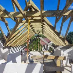 Drewniana konstrukcja dachu w trakcie budowy, widok z wnętrza budynku, jasne niebo w tle.