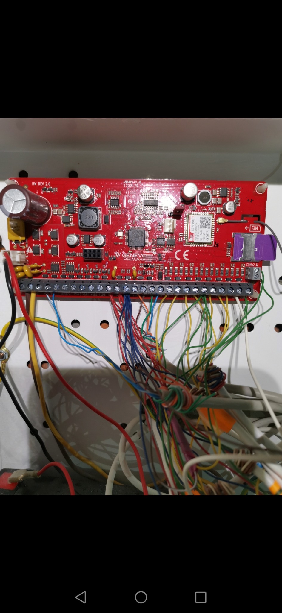 Czerwona płyta główna alarmu Genevo Prima+ z podłączonymi przewodami, widoczny slot na kartę SIM i oznaczenia CE.