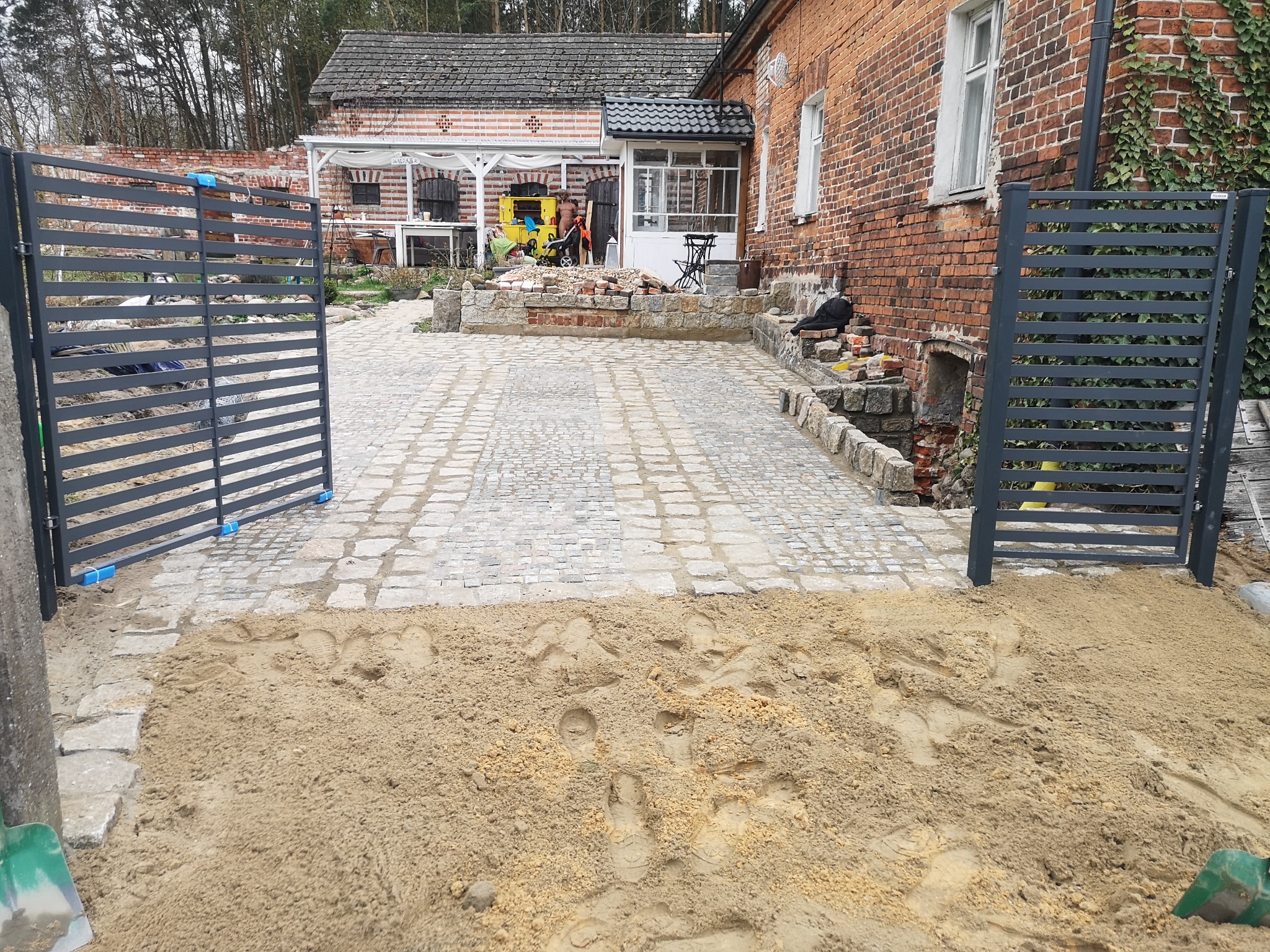 Fragment posesji we Wschowie z podjazdem z kostki granitowej w trakcie układania, widoczny piasek i brama wjazdowa.