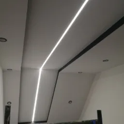 Sufit podwieszany z liniowym oświetleniem LED, widoczny fragment rusztowania malarskiego z niebieską taśmą zabezpieczającą.