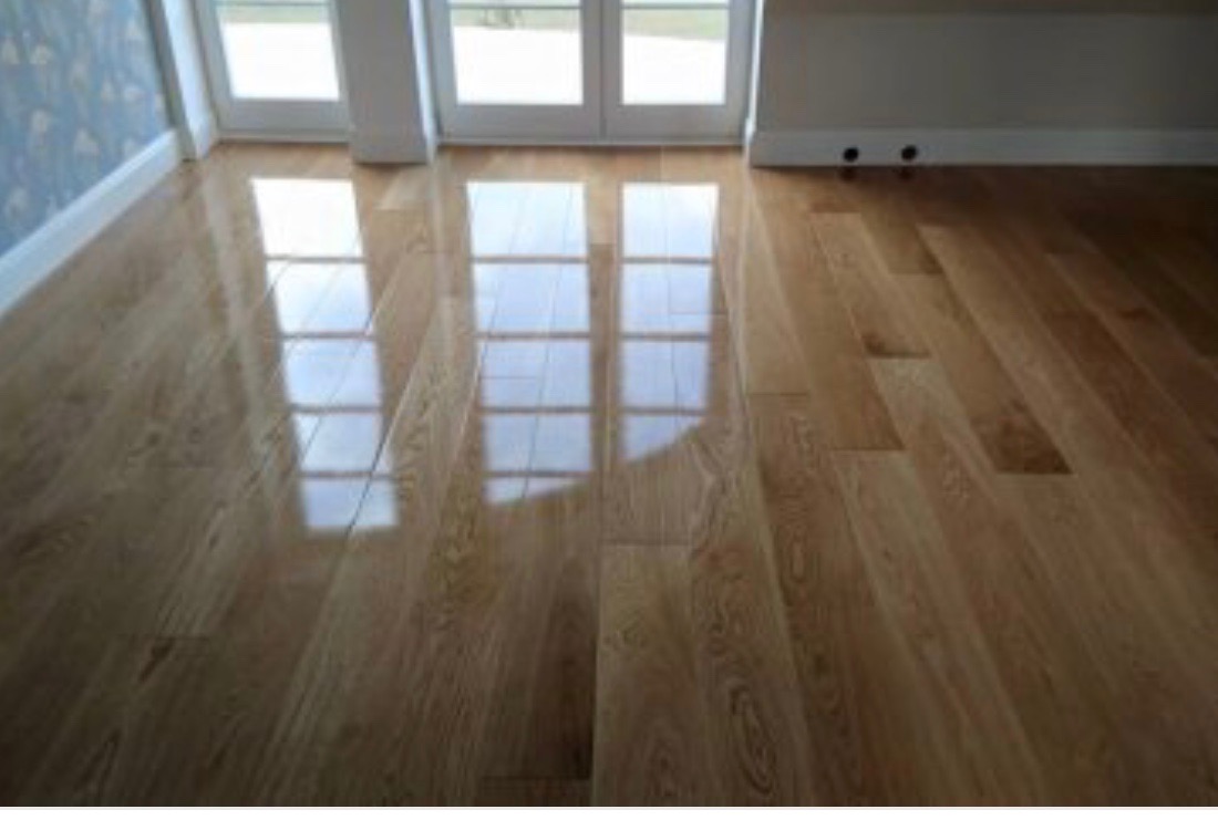 Błyszcząca, świeżo położona drewniana podłoga parkietowa odbija światło z okna, ukazując widoczne łączenia i naturalny rysunek drewna.