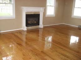 Błyszcząca, świeżo polakierowana podłoga z desek w salonie z kominkiem. Widoczne refleksy światła na gładkiej powierzchni. Jasne ściany i biała obudowa kominka.