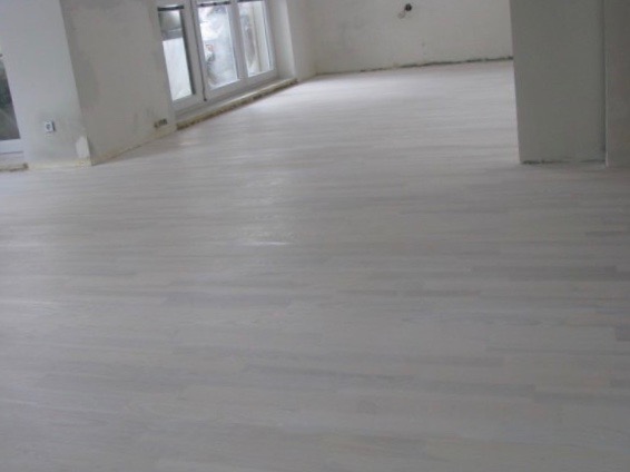 Jasnoszara, świeżo położona podłoga z desek w pustym pokoju z oknami i białymi ścianami w trakcie remontu.