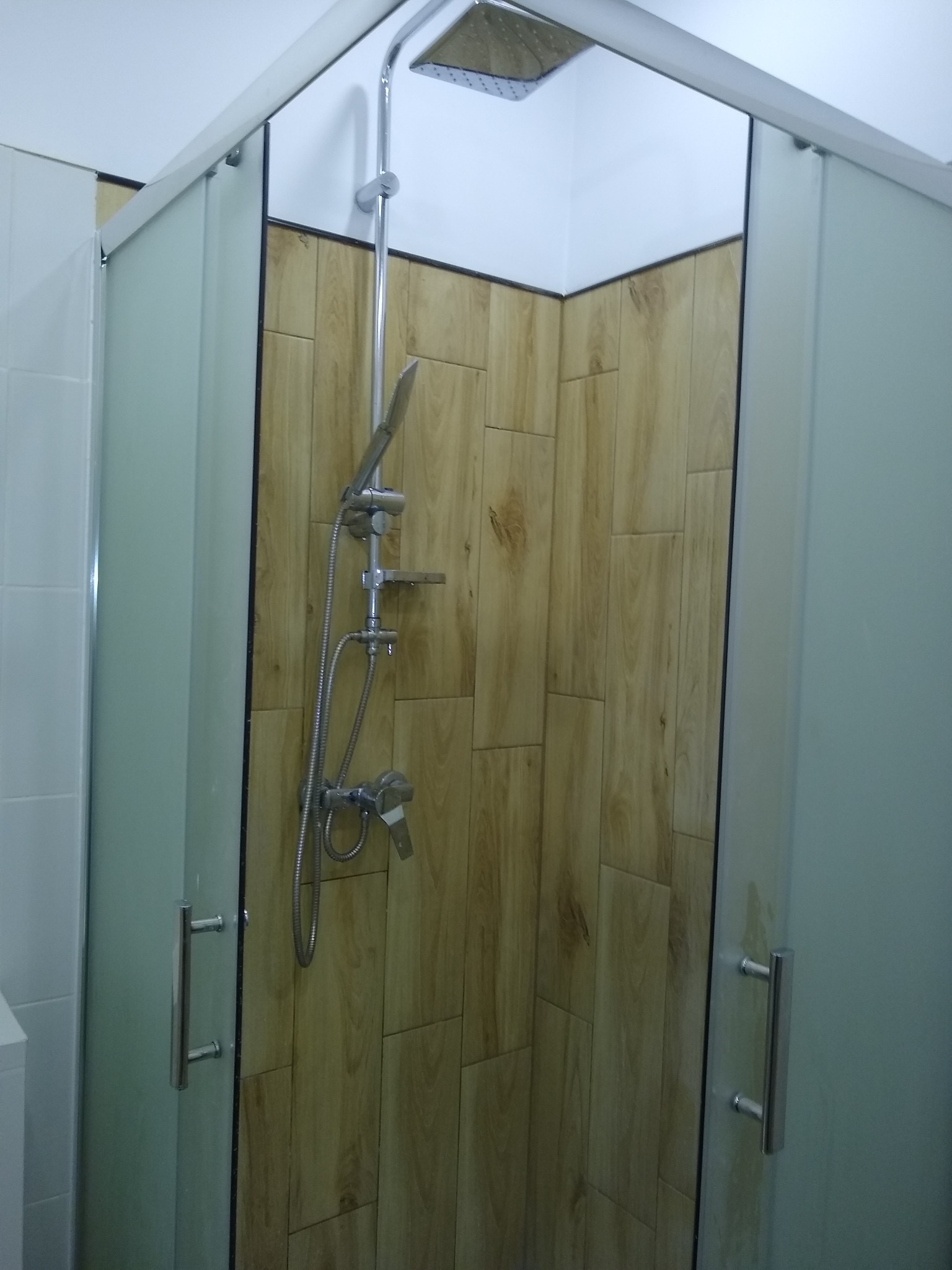 Kabina prysznicowa z drewnopodobnymi płytkami na ścianach, chromowana bateria i deszczownica, matowe szyby kabiny.