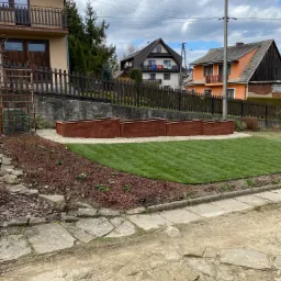 Świeżo założony trawnik z rolki, obrzeża z kory, drewniane donice i kamienne ścieżki w przydomowym ogrodzie.