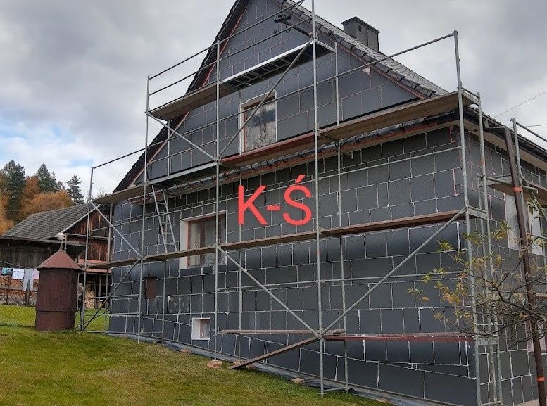 Dom w trakcie ocieplania, ściany pokryte grafitowymi płytami izolacyjnymi, rusztowanie metalowe, widok na boczną ścianę budynku.