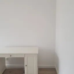 Pusta, biała ściana z drewnianą podłogą i biurkiem w stylu retro z gniazdkiem elektrycznym pod blatem, wnętrze po malowaniu.