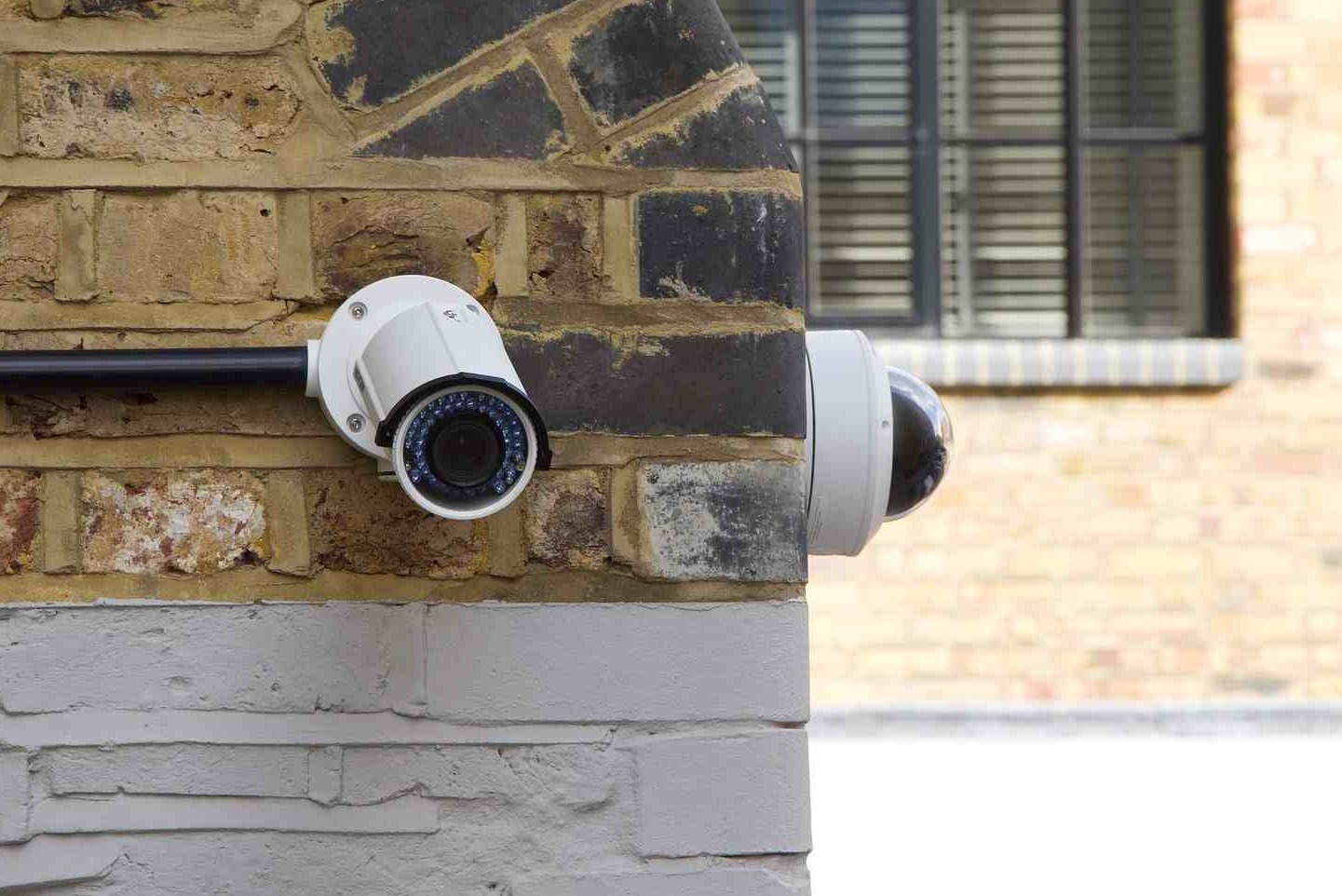 Dwie kamery monitoringu na zewnętrznej ścianie budynku z cegły, jedna z obudową kopułkową, druga z widocznymi diodami IR.