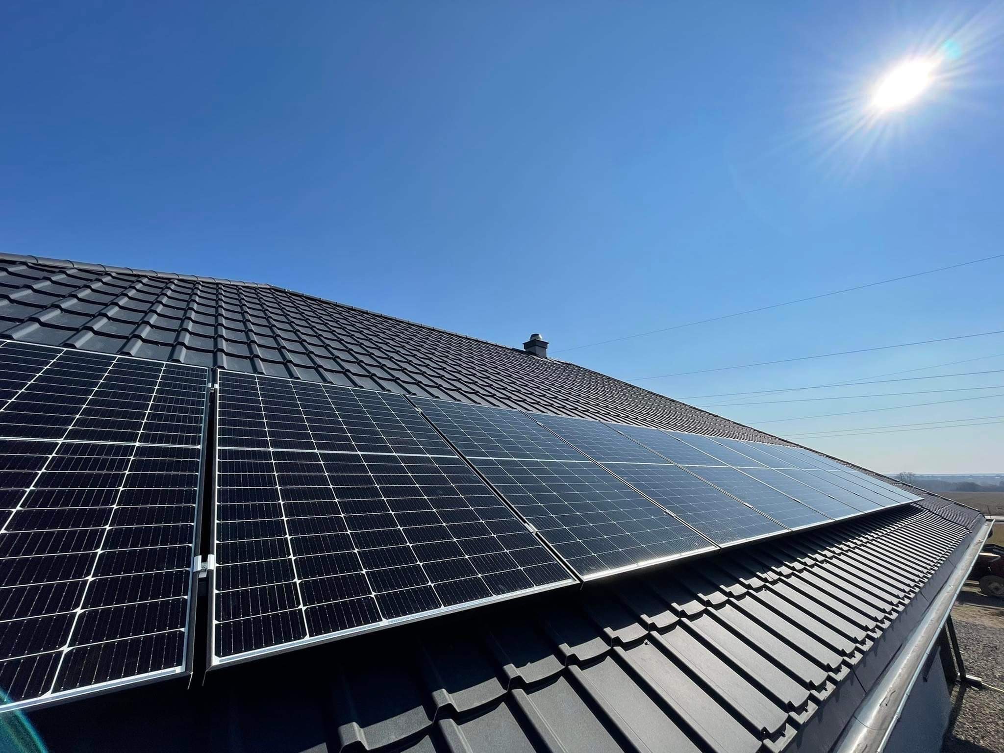 Panele słoneczne zamontowane na dachu z czarnej dachówki ceramicznej, widok z dołu pod kątem, błękitne niebo w tle.