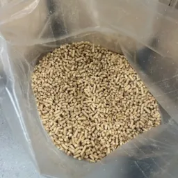 Wnętrze przezroczystego worka wypełnionego jasnymi, cylindrycznymi granulkami opału, widoczny fragment niebieskiego buta w dolnym rogu.