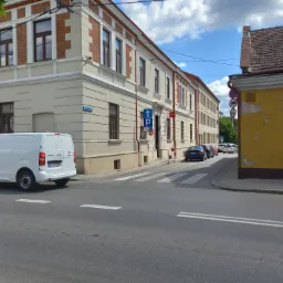 Biały samochód dostawczy marki Peugeot Expert zaparkowany na ulicy w pobliżu skrzyżowania z budynkami w tle.