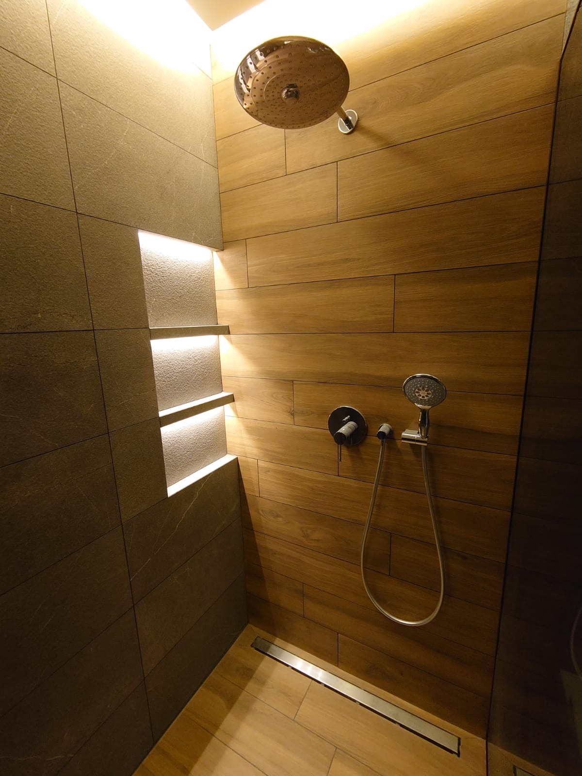 Nowoczesny prysznic walk-in z drewnopodobnymi płytkami na ścianach, deszczownicą sufitową i wnęką z oświetleniem LED.