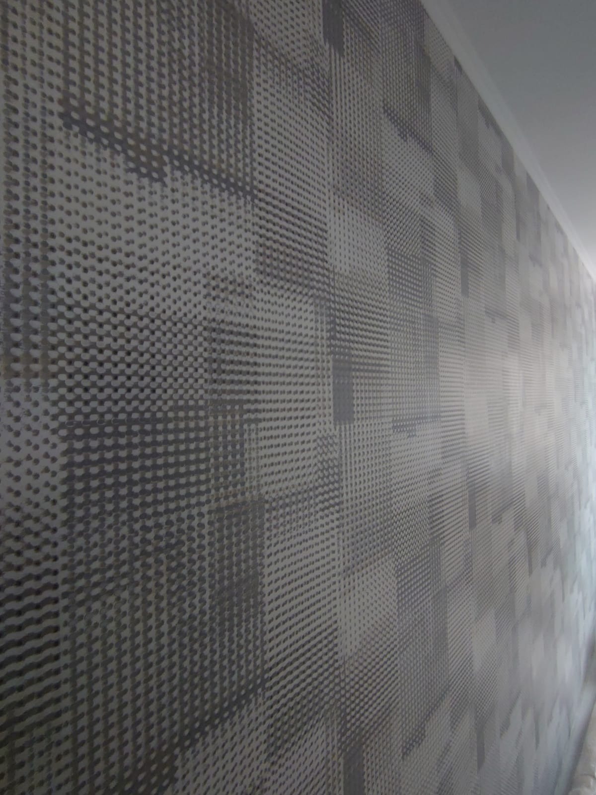 Ściana pokryta tapetą z geometrycznym wzorem w odcieniach szarości, z bliska, widoczna listwa przypodłogowa.