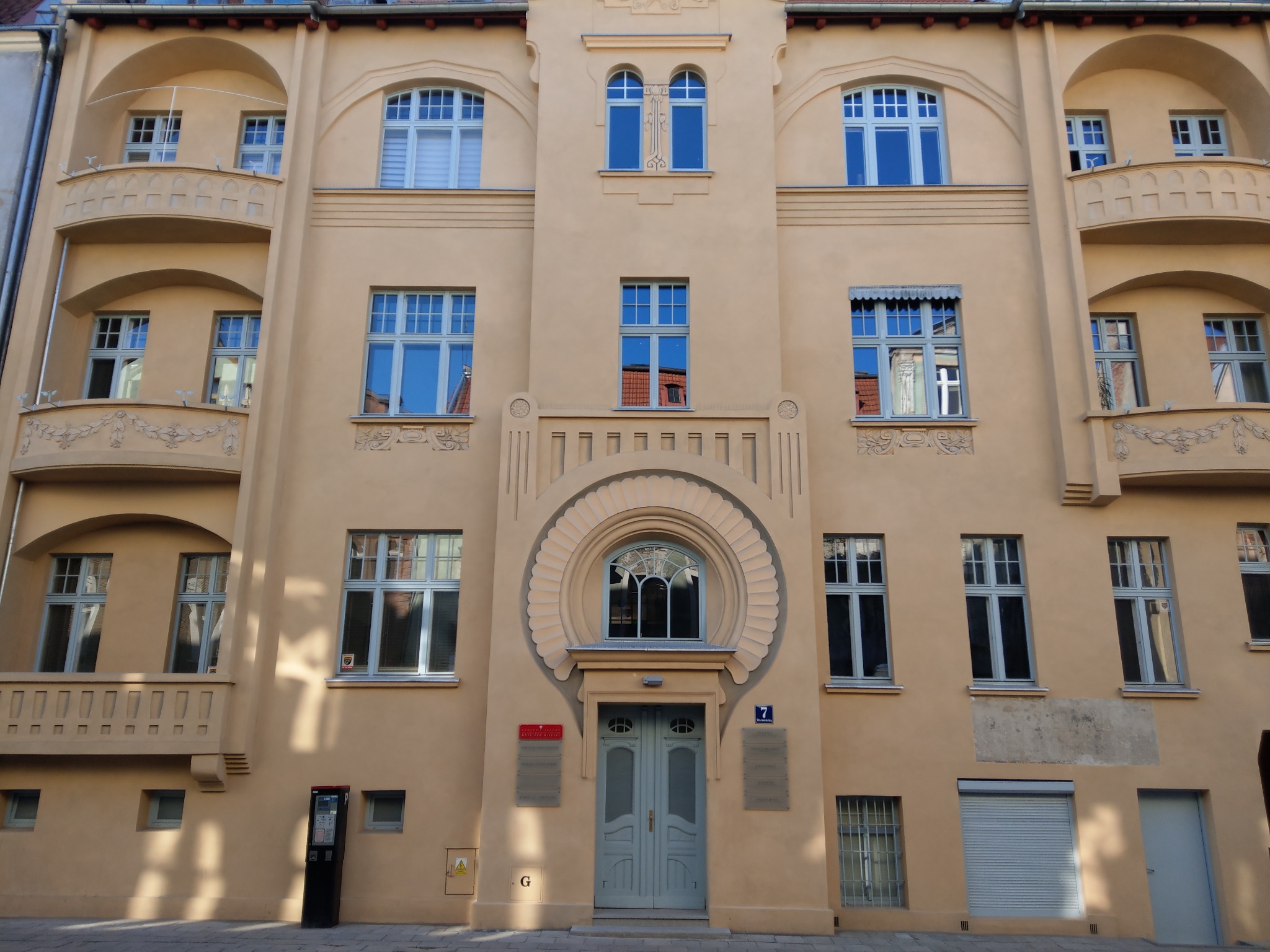 Elewacja kamienicy w stylu secesyjnym z niebieskimi oknami, balkonami i ozdobnym portalem wejściowym