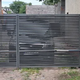 Nowoczesna, dwuskrzydłowa brama wjazdowa z poziomych profili stalowych, zautomatyzowana, widok z zewnątrz na tle budynku z kwiatami w doniczce.