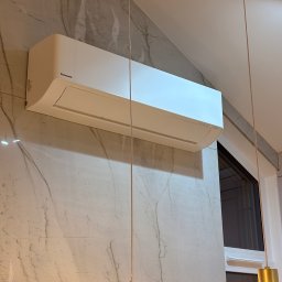 SparBud - Biała klimatyzacja Panasonic zamontowana na ścianie z marmurowym wzorem, widoczna z dołu, z elementami oświetlenia w kadrze. Nowoczesny design.