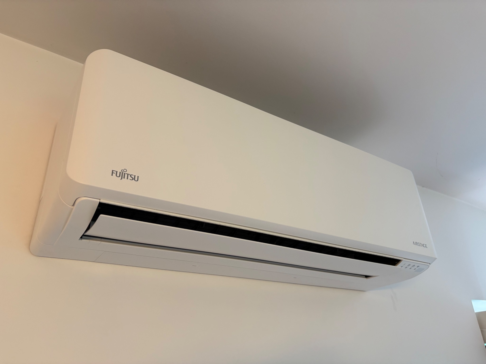 Biała klimatyzacja Fujitsu Airstage, zamontowana na jasnej ścianie. Widoczne logo i panel sterowania. Minimalistyczny design w nowoczesnym wnętrzu.