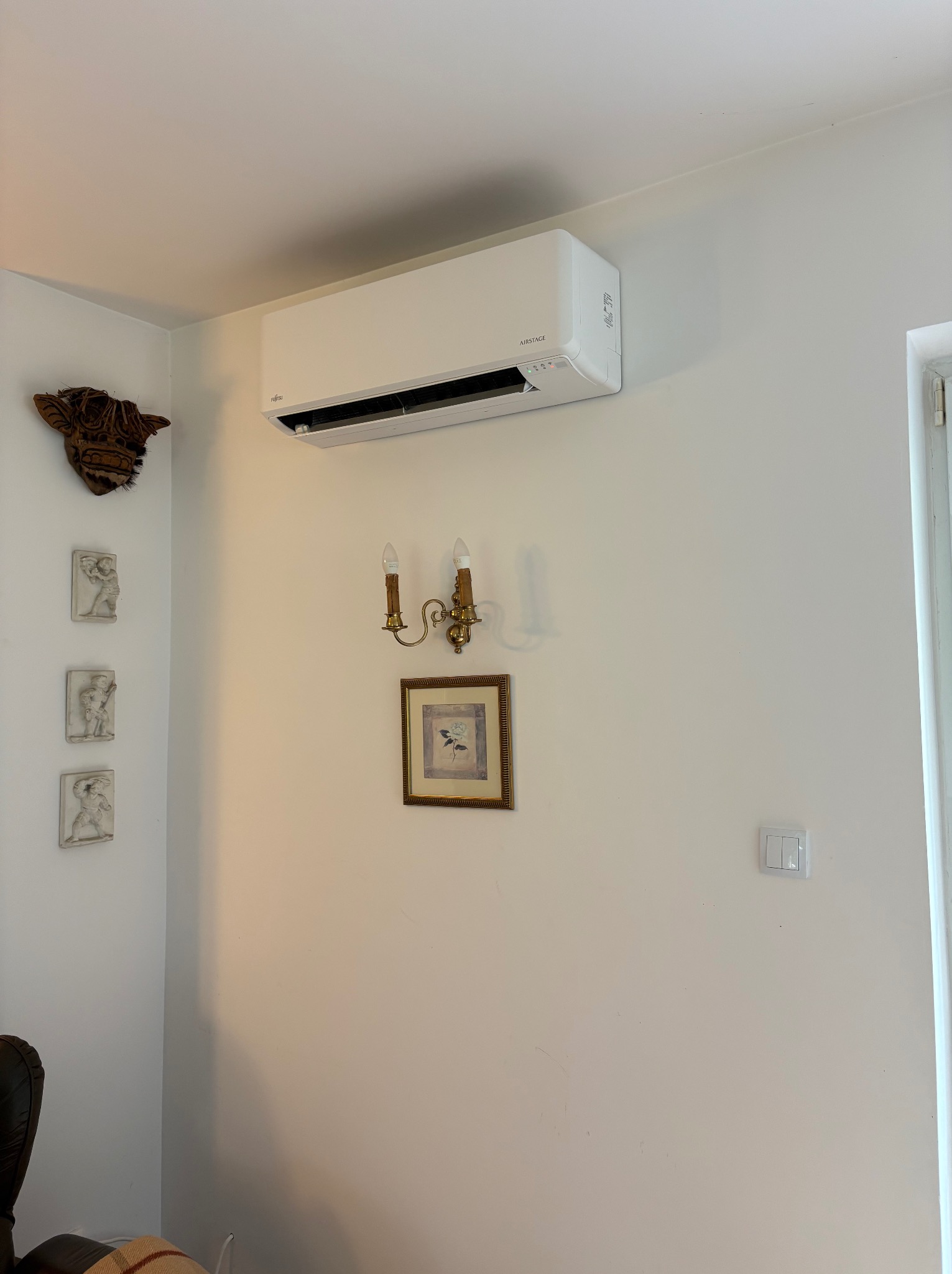 Zamontowany klimatyzator AIRSTAGE na białej ścianie w pokoju z dekoracjami, w tym maską, płaskorzeźbami i kinkietem.