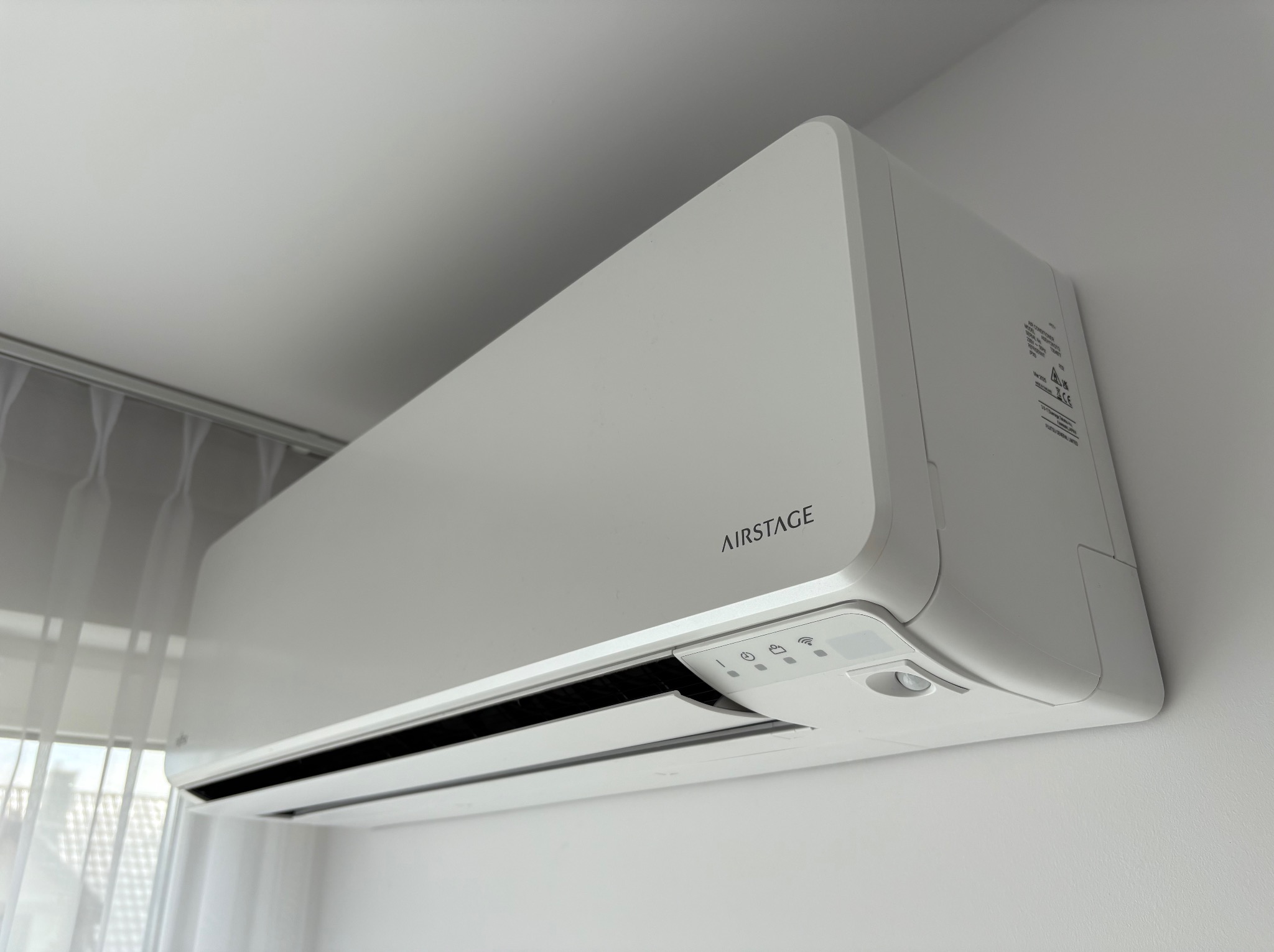 Nowoczesny, biały klimatyzator Airstage zamontowany na ścianie, widok z dołu, z subtelnym oświetleniem z okna w tle. Minimalistyczny design.