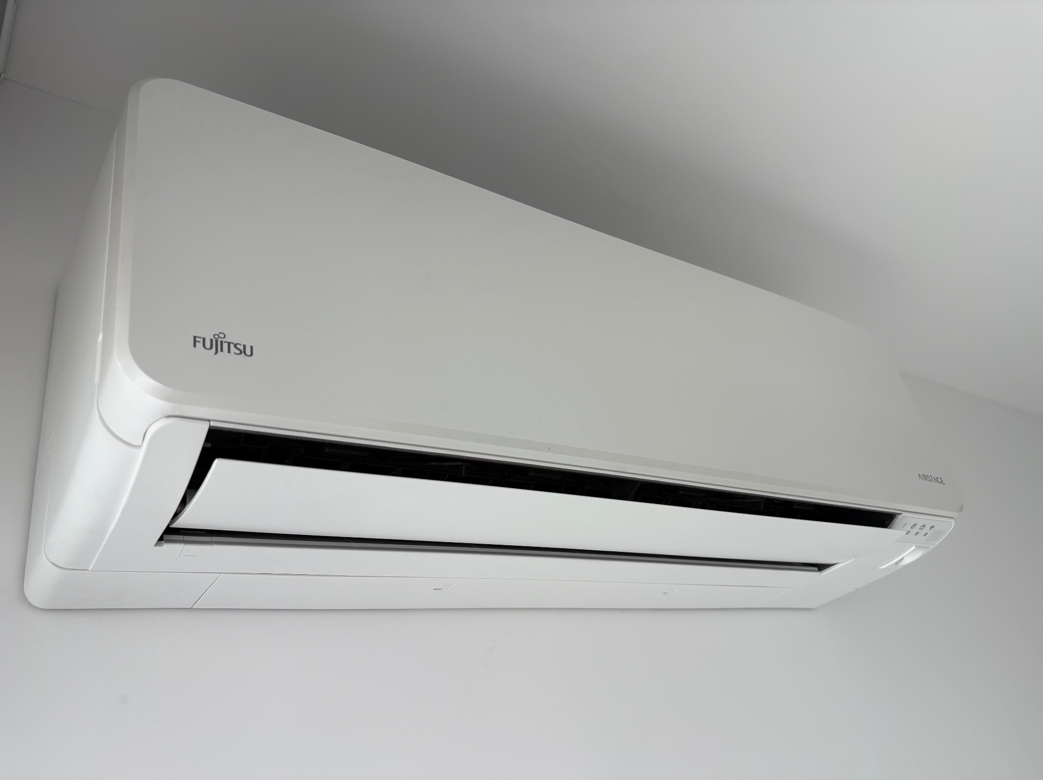 Biała klimatyzacja Fujitsu Airstage zamontowana na ścianie, widoczna z dołu pod kątem. Minimalistyczny design i czyste linie urządzenia.